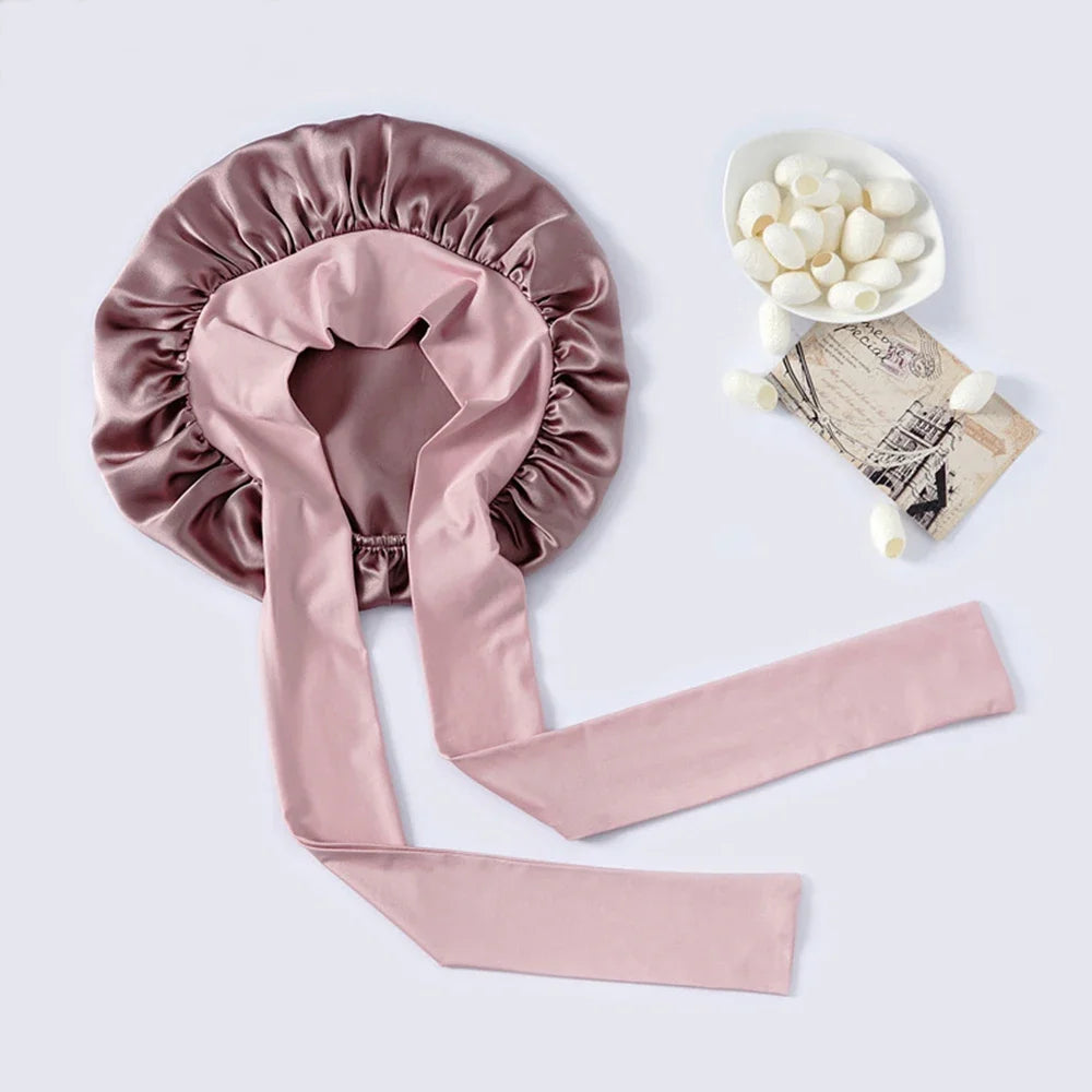 A pink mulberry silk sleep bonnet with a satin ribbon and a bowl of white hair accessories.