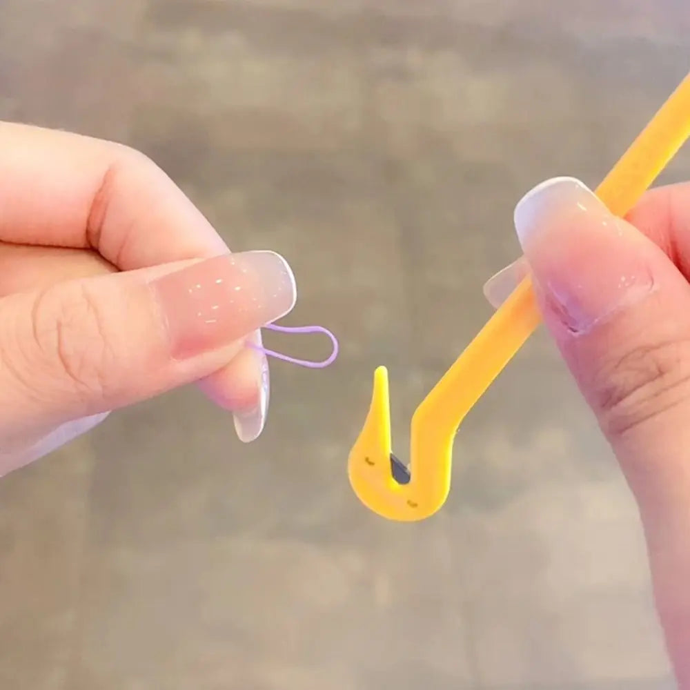 A hand is using a yellow tool to remove a purple elastic band from a fingernail.