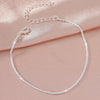 A delicate silver-plated chain anklet adorned with clear cubic zirconia stones, displayed on a pink fabric.