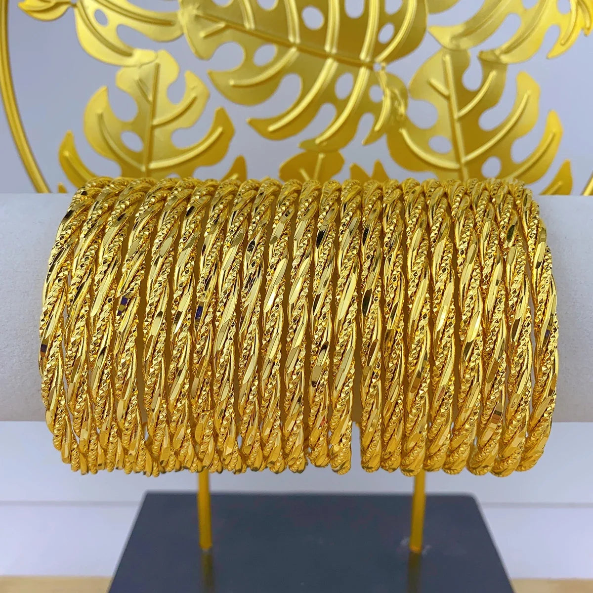 Spule aus 24K-Goldfarbenen geometrischen Armreifen vor goldenem Blattgrund.
