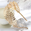 A delicate gold leaf headband featuring a fern design resting on a white surface.