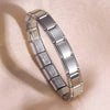 A silver stainless steel charm bracelet is displayed on a light pink background.