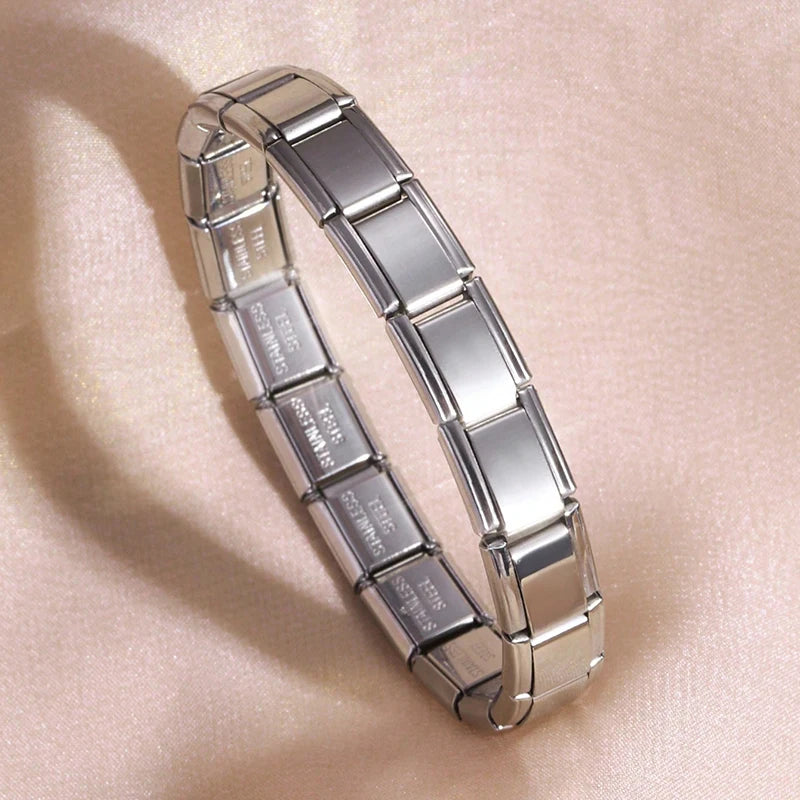 A silver stainless steel charm bracelet is displayed on a light pink background.