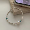 A sterling silver double heart charm bracelet with small pearls and turquoise beads resting on a light-colored surface.