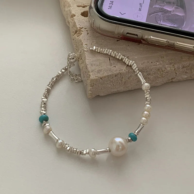A sterling silver double heart charm bracelet with small pearls and turquoise beads resting on a light-colored surface.