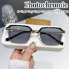 Une paire de lunettes de lecture photochromiques avec des montures dorées et des verres foncés posées sur une boîte blanche.