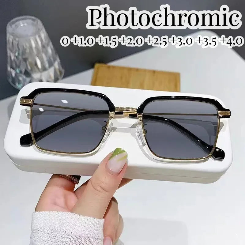 Une paire de lunettes de lecture photochromiques avec des montures dorées et des verres foncés posées sur une boîte blanche.