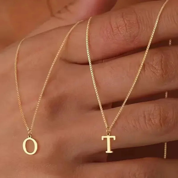 Nahaufnahme einer goldvergoldeten Initialkette mit feiner Kette und einem Buchstaben T, getragen an der Hand.