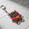 A clear plastic keychain featuring a black cat face with orange eyes and an orange belt detail.