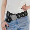 A close-up of a woman wearing a black and silver vintage western denim belt over a white top and blue jeans.