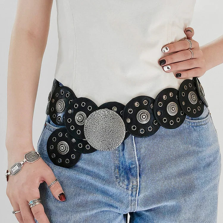 A close-up of a woman wearing a black and silver vintage western denim belt over a white top and blue jeans.