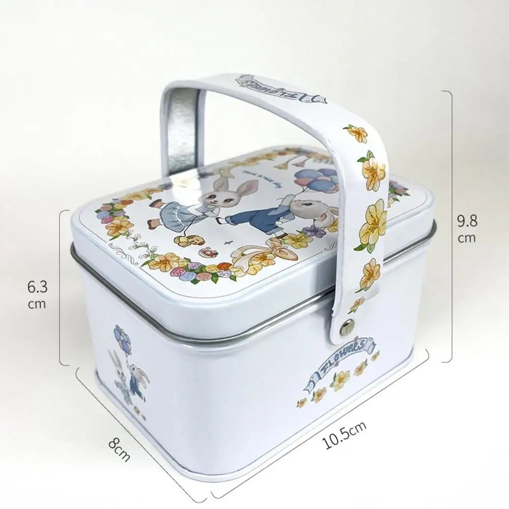 A white tinplate candy box with a decorative floral pattern and a handle.