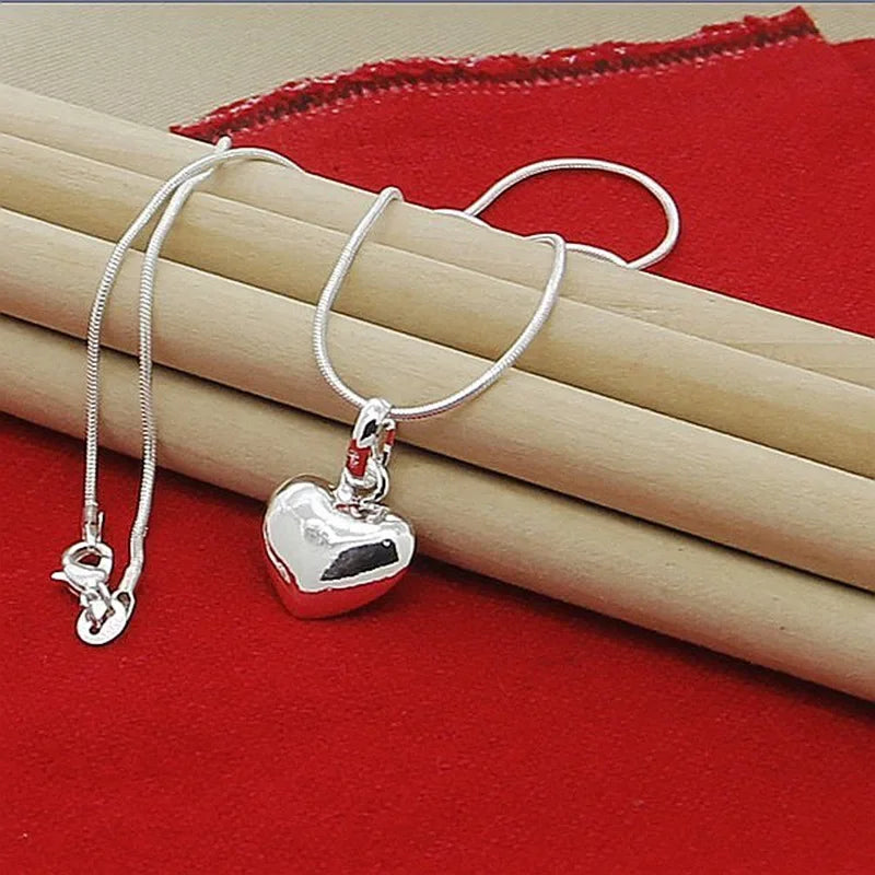 A silver heart snake necklace is displayed on a red velvet fabric next to a wooden surface.