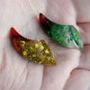 Two silicone molds shaped like devil horns or claws, featuring green and gold glitter finishes, resting on a hand.