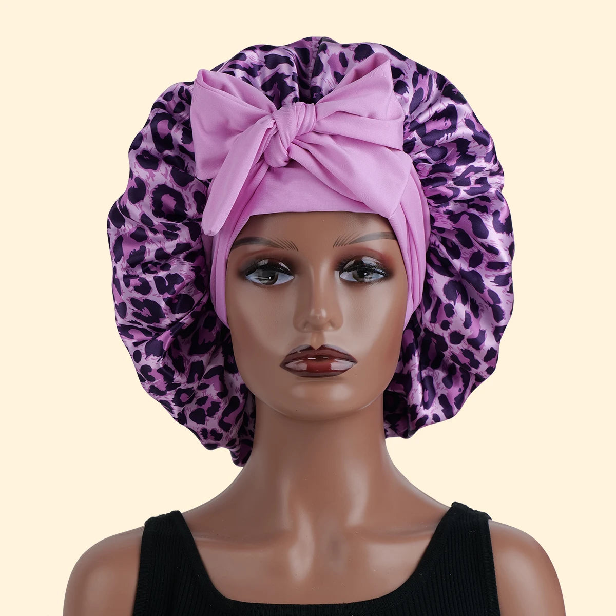 A model wears a pink leopard print satin sleep bonnet on her head.