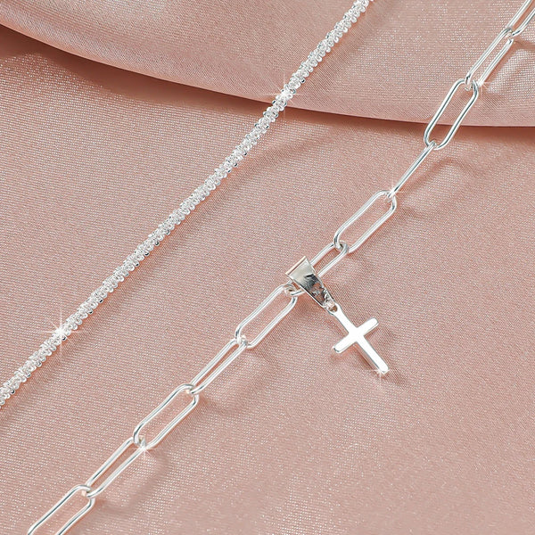 Silver plated CZ anklet chain and cross pendant displayed on a pink fabric background