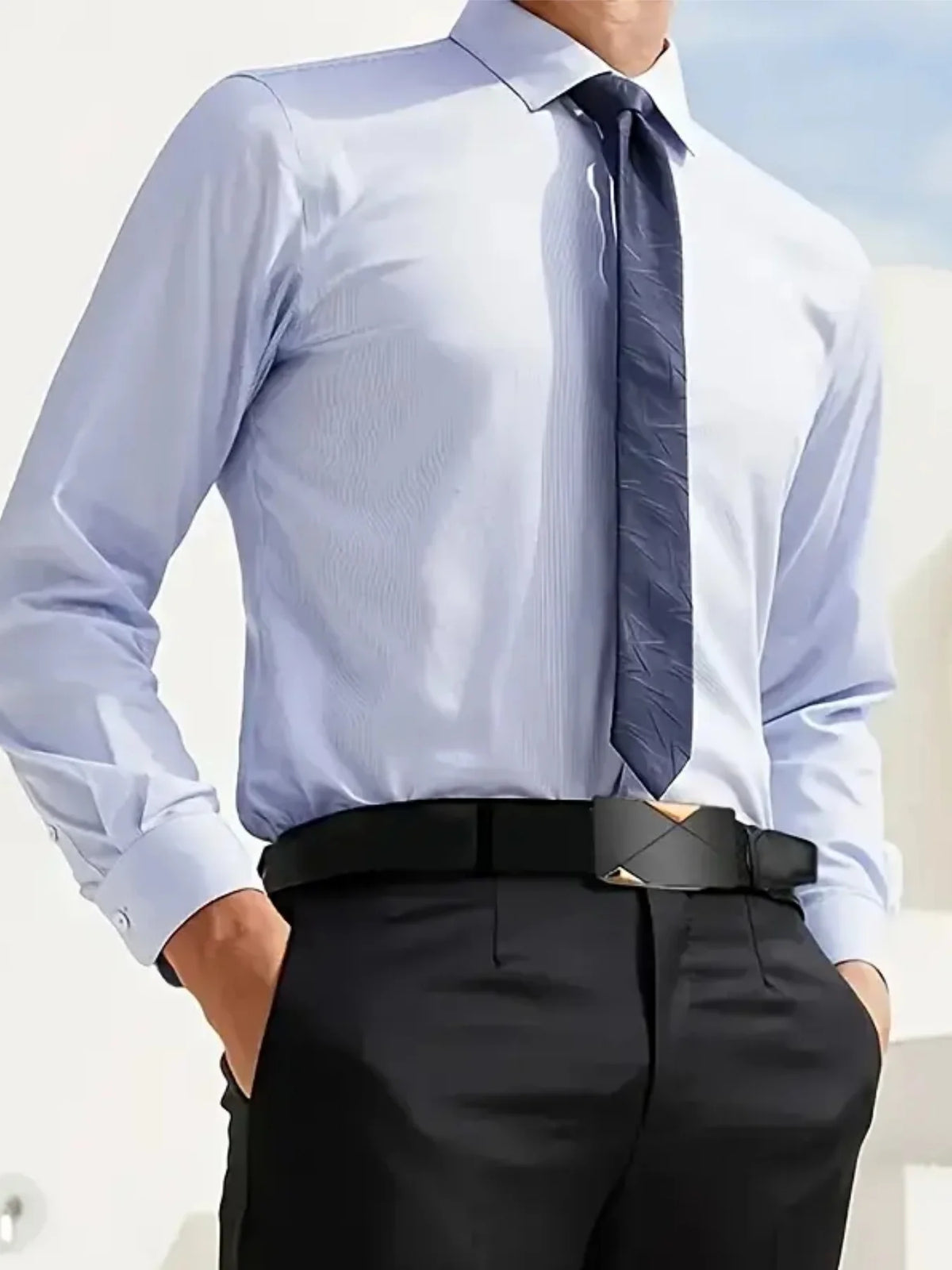 A man wearing a light blue dress shirt, dark tie, and black trousers with a black buckle belt.