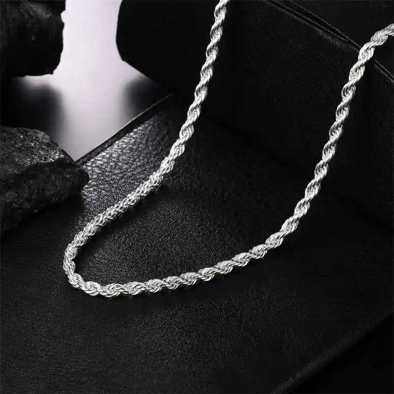 A silver rope charm necklace is displayed on a black leather surface.
