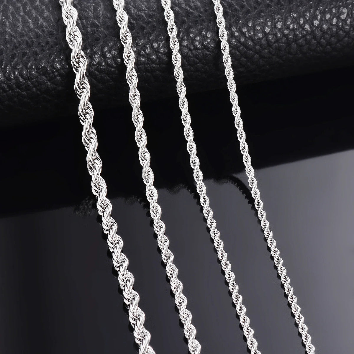 Primer plano de un collar de cadena de cuerda plateada colgando contra un fondo oscuro.