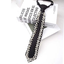 A black neck tie adorned with a string of white pearls and rhinestones, displayed next to a book.