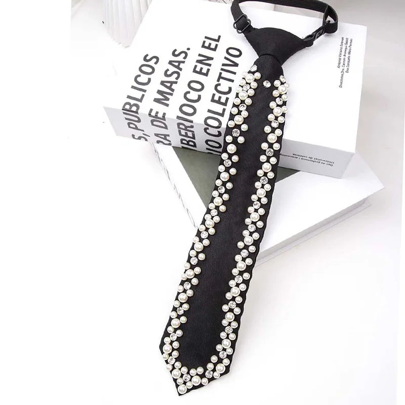 A black neck tie adorned with a string of white pearls and rhinestones, displayed next to a book.