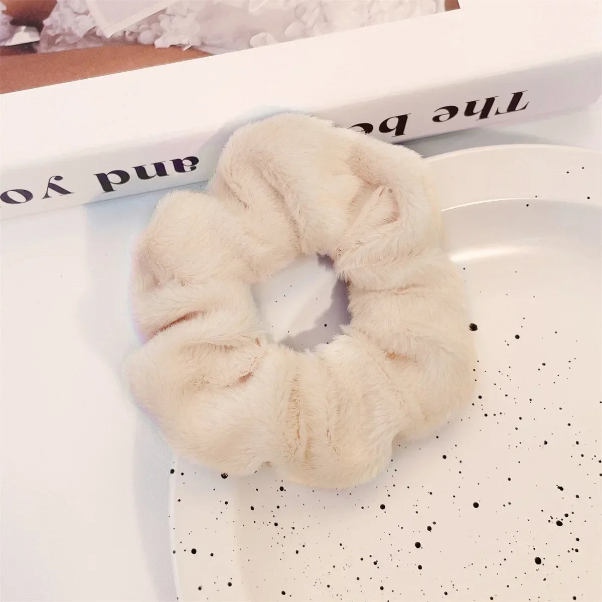 Scrunchie en tricot flou de couleur crème sur une assiette blanche à pois noirs.