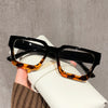 A pair of black square anti-blue light computer glasses resting on a white surface.