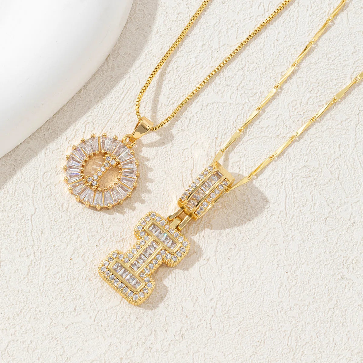 Gold-toned necklace set featuring CZ crystal pendants shaped like letters, displayed on a light background.