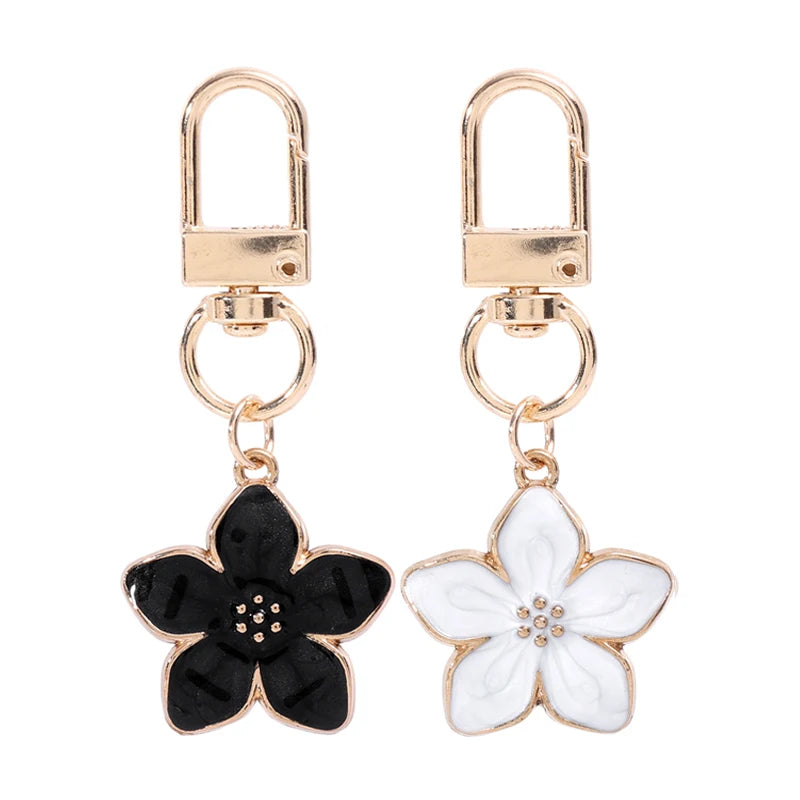 Un par de llaveros florales en tono dorado con diseño de flor en blanco y negro.