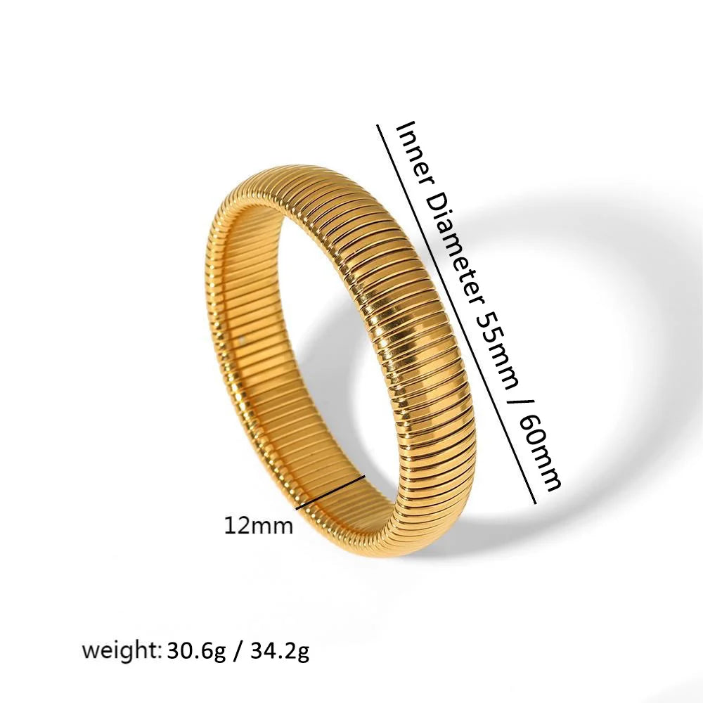 A close-up view of a gold-toned elastic bangle bracelet with a textured finish and a measurement scale.