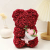 Un bouquet de roses en mousse rouge foncé en forme d'ours en peluche, exposé à côté d'une lampe.