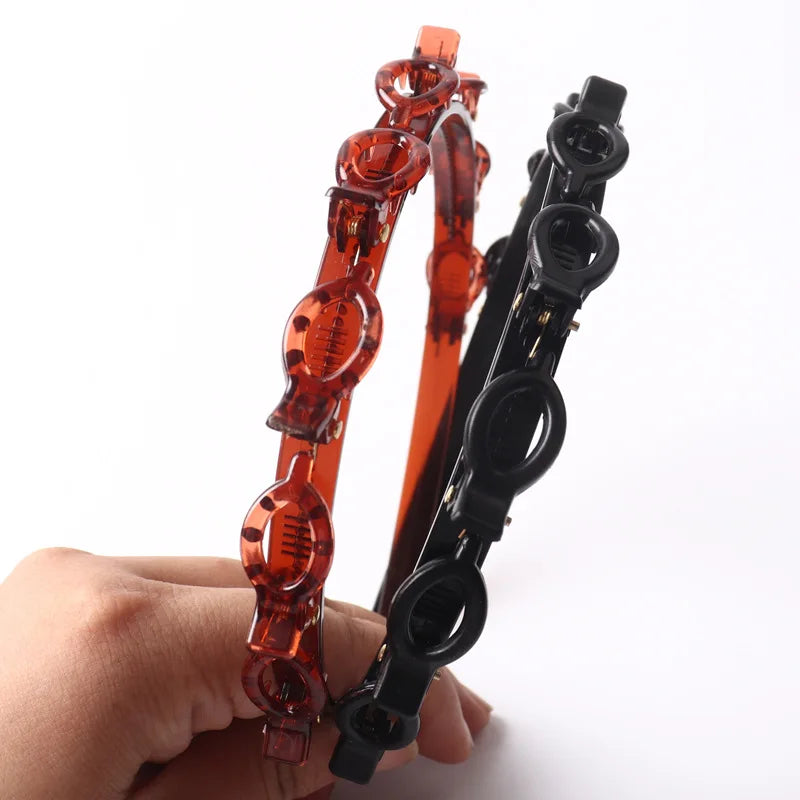 A hand holds a multi-layer braided hair headband clip in orange and black.