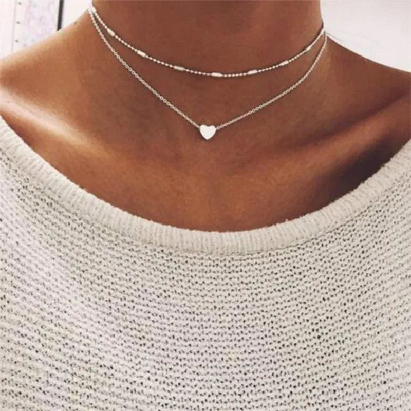 Gros plan d'une femme portant un collier de perles minimaliste superposées sur un fond neutre.