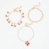 A set of gold-toned anklets featuring delicate chains and small red cherry beads.