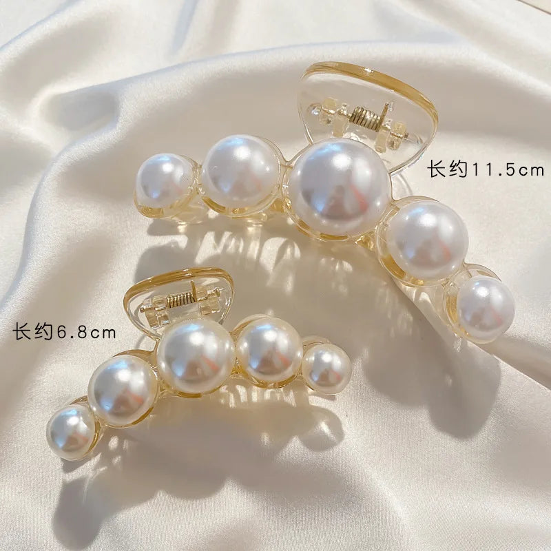 A pair of simulated pearl hair claws, one measuring 11.5cm and the other 6.8cm, displayed on a white satin fabric.