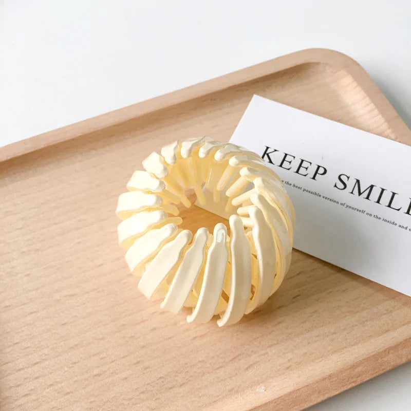 A close-up of elegant horsetail hair clips in a creamy yellow color resting on a wooden tray next to a card.