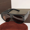 Black oversized pilot sunglasses resting on a brown box and a reddish-brown fabric.