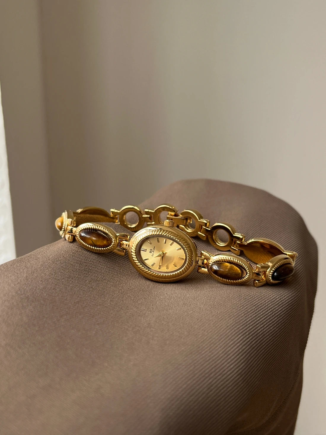 Montre de couleur or avec cadran jaune clair et perles marron, présentée sur une surface neutre.