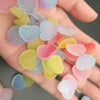 A hand holds a collection of colorful, heart-shaped resin nail art charms in various pastel shades.