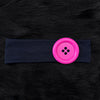 A bright pink wind dot stretch hairband fastened with a button, resting on a dark blue fabric band.