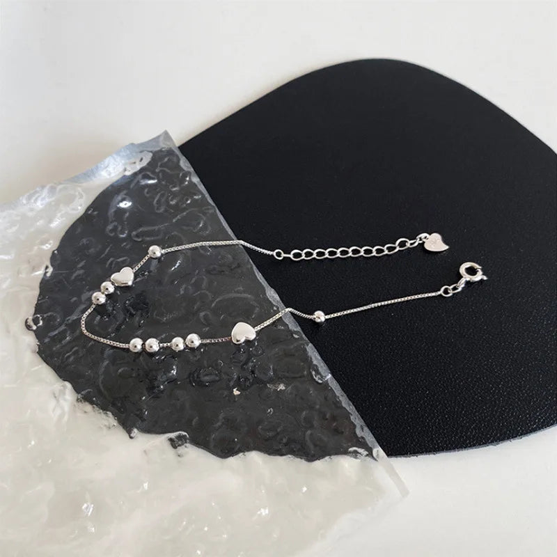 Sterling silver double heart charm bracelet displayed on a black surface next to a piece of rough white stone.