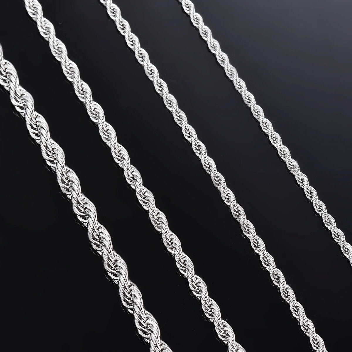 Primer plano de varias cadenas de collar de cuerda plateada dispuestas en diagonal sobre una superficie oscura.