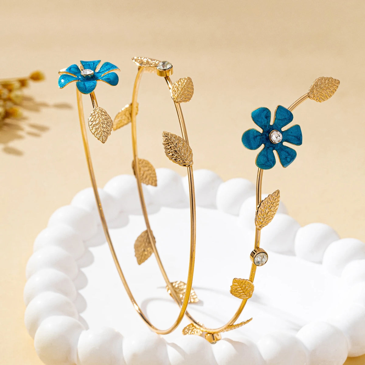 Gold floral vine arm bracelet with blue enamel flowers and small gold leaves displayed on a white surface