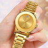 Una mano sostiene un reloj de cuarzo dorado con esfera redonda y pulsera de eslabones dorados.
