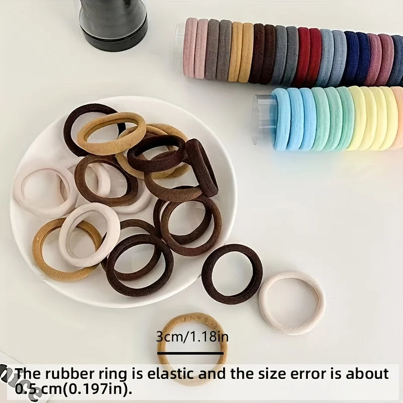 A collection of various colored rubber rings and elastic hair ties are displayed on a white plate and next to a row of stacke