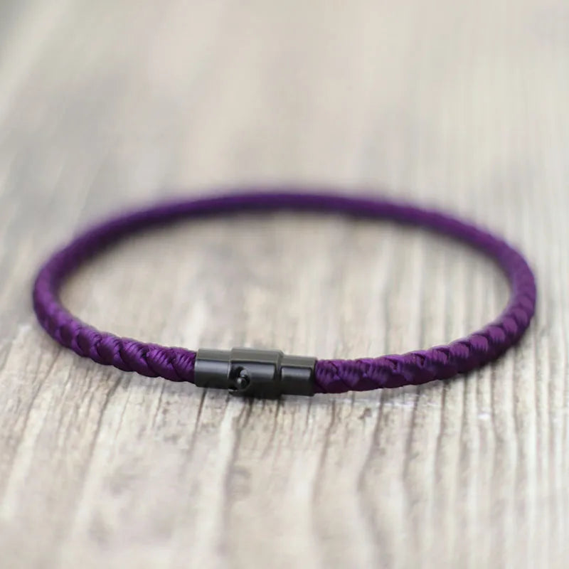 Purple thread charm bracelet with a black clasp resting on a light wooden surface.