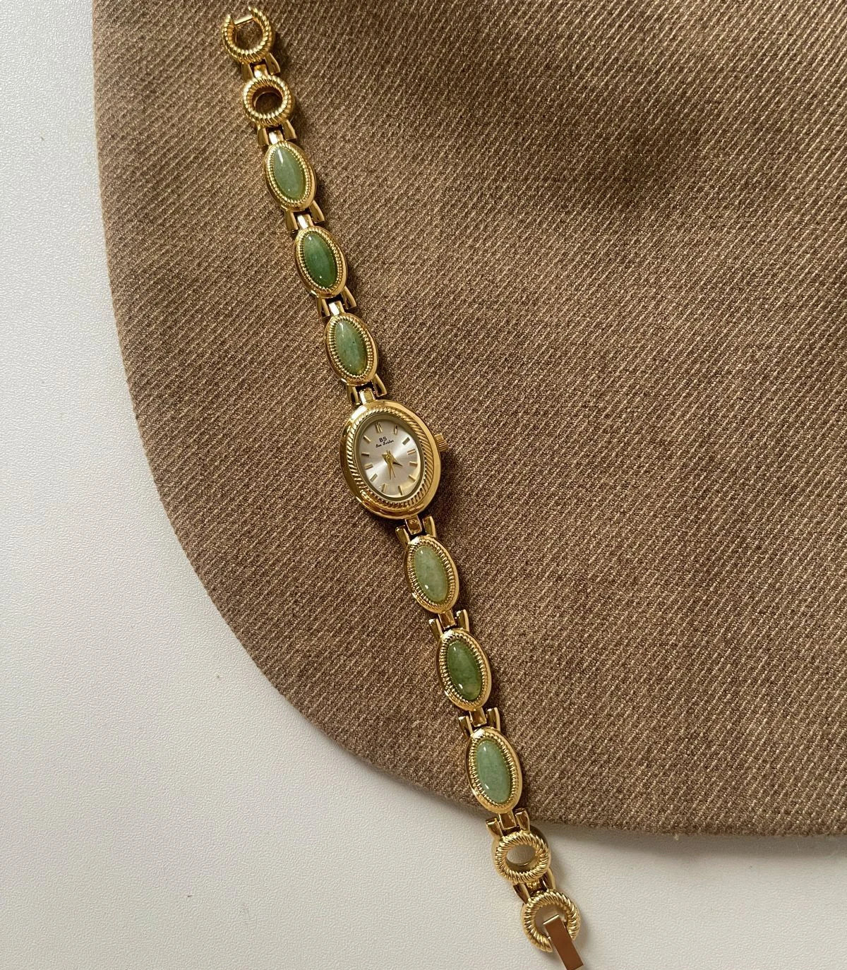 Montre en quartz jade vert élégante avec chaîne dorée sur fond de tissu beige.