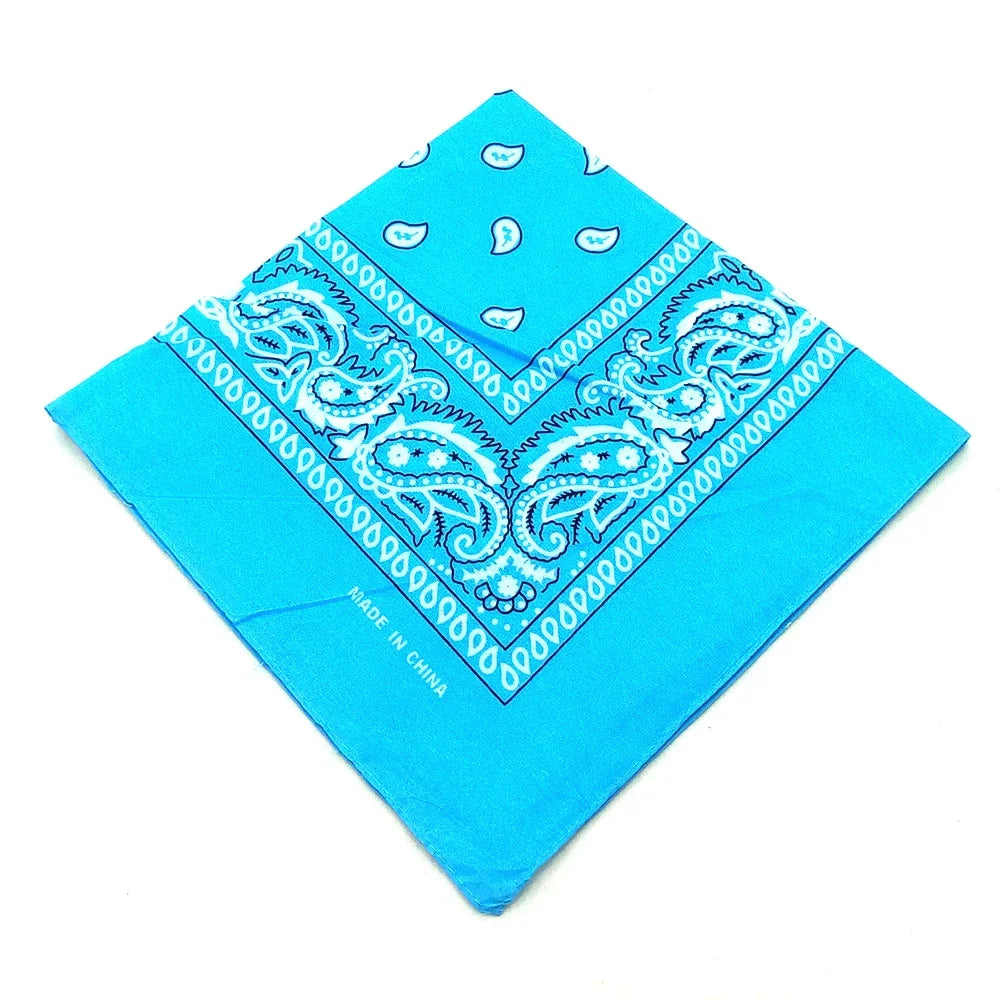 A bright blue bandana featuring intricate white paisley and floral patterns, folded into a diamond shape.