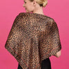 A woman models an elegant floral satin shawl in brown leopard print against a pink background.