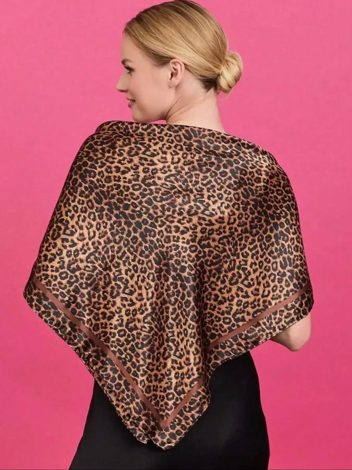 A woman models an elegant floral satin shawl in brown leopard print against a pink background.